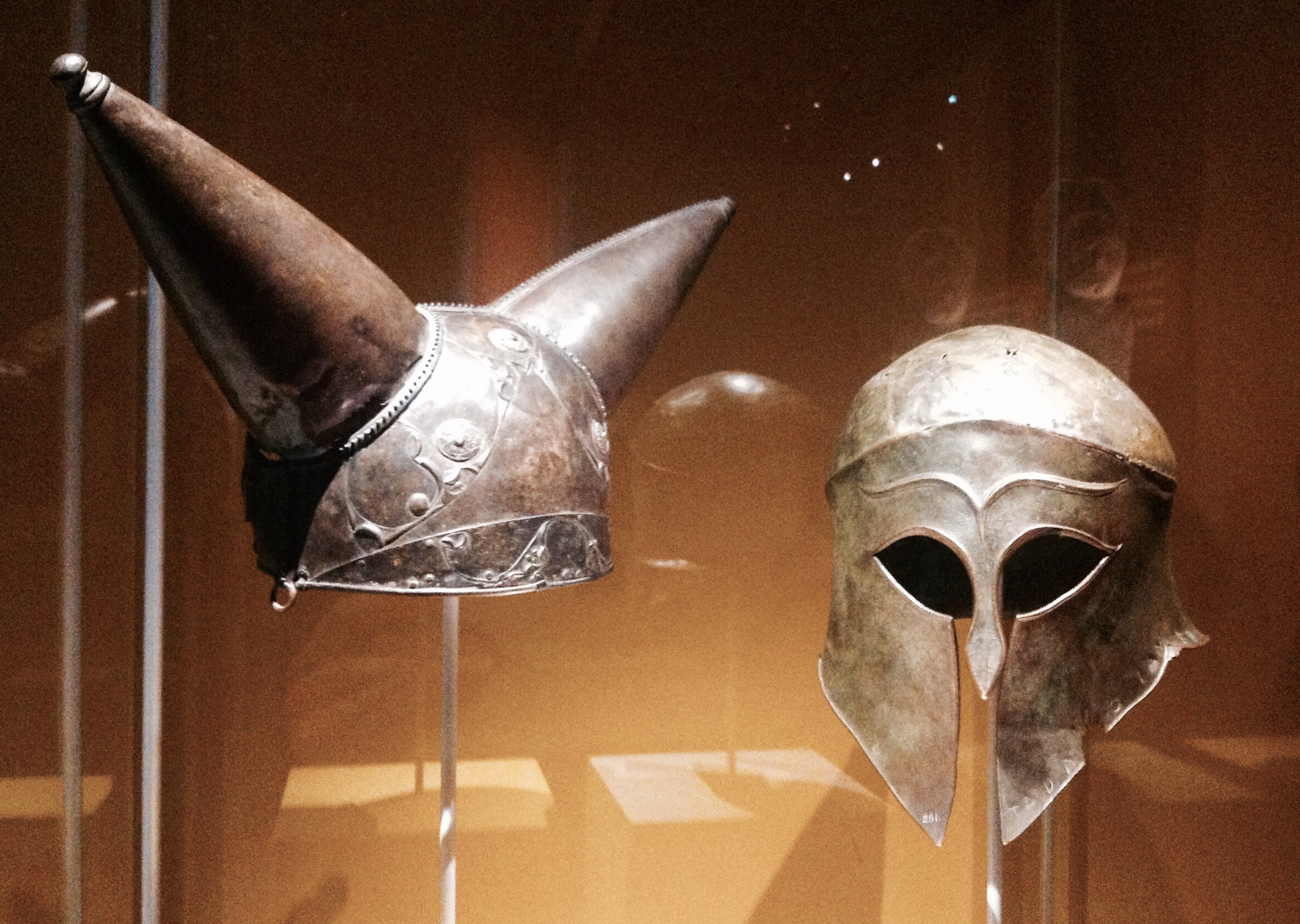 (L) Horned helmet. Bronze, glass, Found along the Thames river near Waterloo, London, England (200-100 BC). (R) Greek helmet, bronze. Olympia, South-Western Greece (460 BC), The British Museum.Photo by Medievalists.net.