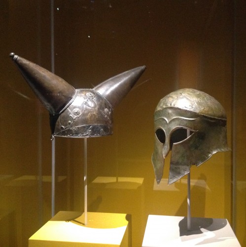 (L) Horned helmet. Bronze, glass, Found along the Thames river near Waterloo, London, England (200-100 BC). (R) Greek helmet, bronze. Olympia, South-Western Greece (460 BC). The British Museum. Photo by Medievalists.net